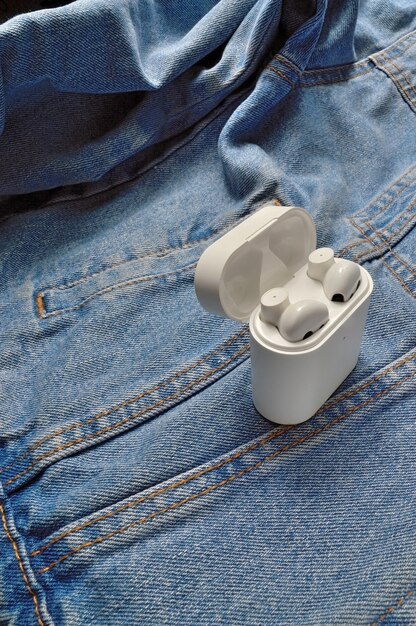 A top-down view of three different models of wireless earbuds cases, each open to reveal the earbuds inside, arranged on a textured grey surface, highlighting their varying sizes and designs.