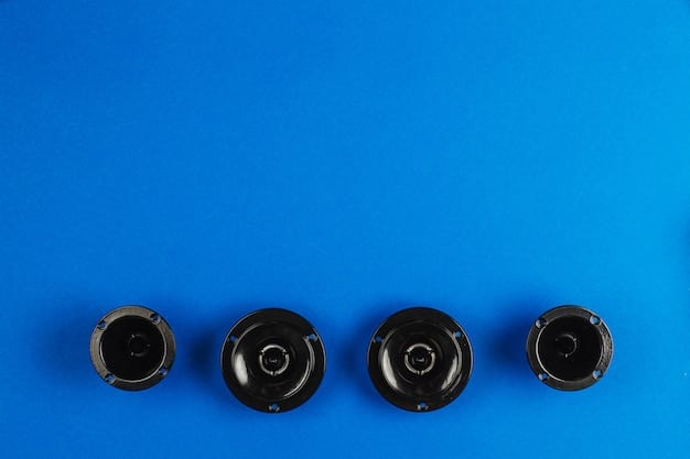 A top-down view of three different Bluetooth speakers (JBL Flip 6, Sony SRS-XB23, and a small, square, generic rugged speaker) arranged neatly on a picnic blanket, surrounded by items like sunglasses, sunscreen, and a book, under bright daylight.